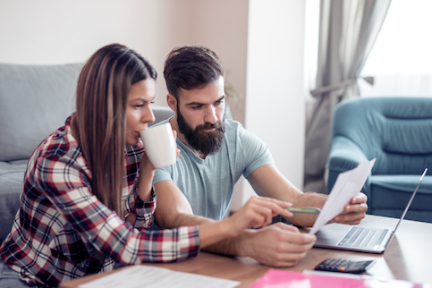 Couple reviewing financial documents together, sitting on couch in living room.