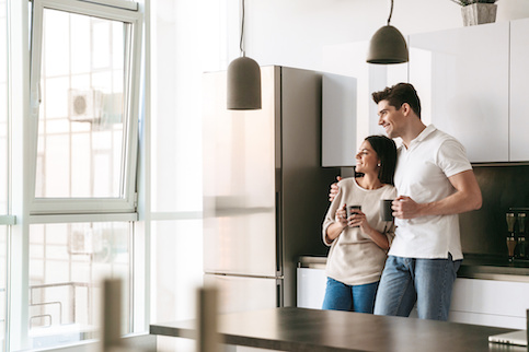 Couple drinking coffee from mugs in a small, modern kitchen.