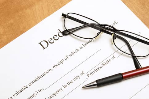 A paper deed on a table with a pen and pair of glasses on top of it.