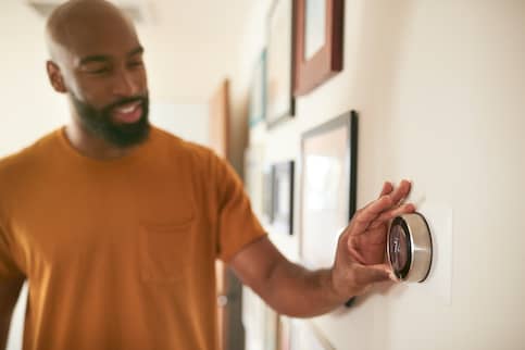 man in orange shirt adjusting energy saving thermostat