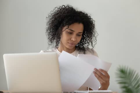 Ethnic Woman Reading Documents And Laptop