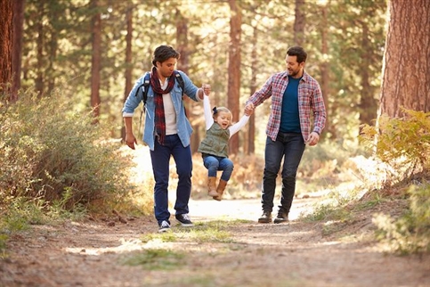 Dads with their daughter on a wooded path in the fall. 