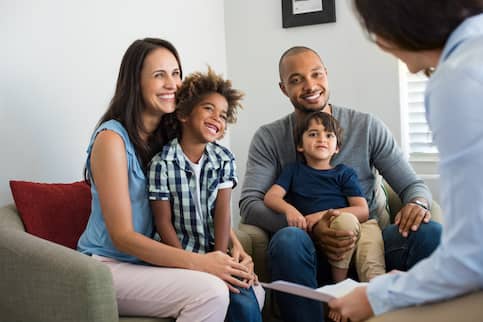 family of 4 sitting in the living room speaking to a woman