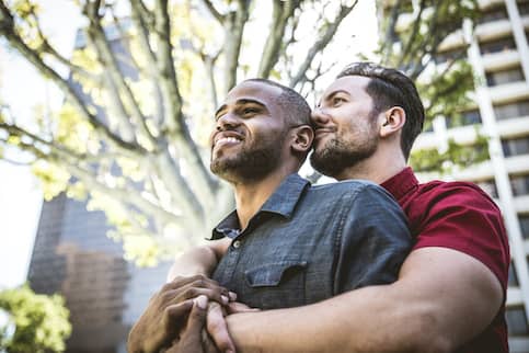 Two men embracing in a park in a city.