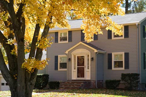 Grey house with yellow tree our front.