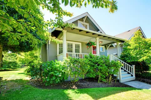 Small grey house with a white porch in spring.