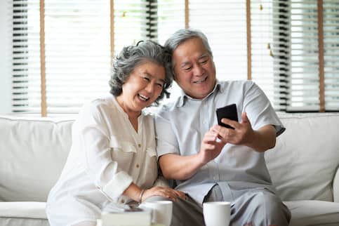 Happy senior Asian couple using their phone on the couch.