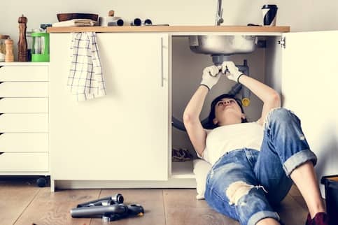 Woman Fixing Kitchen Sink Clog In Her Home 