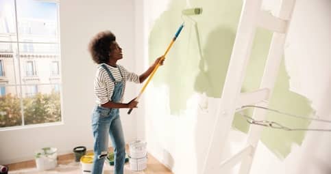 Young African American Woman Painting Wall Of Fixer Upper For House Flipping