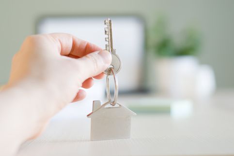 Hand holding key with house shaped keychain.