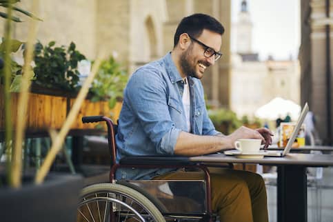 Man in wheelchair at coffee table on laptop.