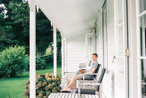 Man sitting on front porch of his new house drinking a glass of wine.