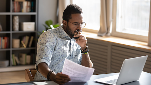 Man looking at paperwork and his laptop.