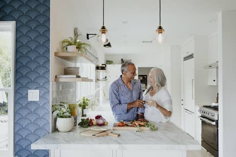 Retired Older Married Couple Cooking In Open Style Kitchen Drinking Wine