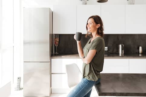 Woman drinking coffee in kitchen of new home she negotiated best home price on.