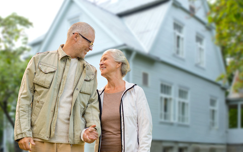 Older couple holding hands outside their house.