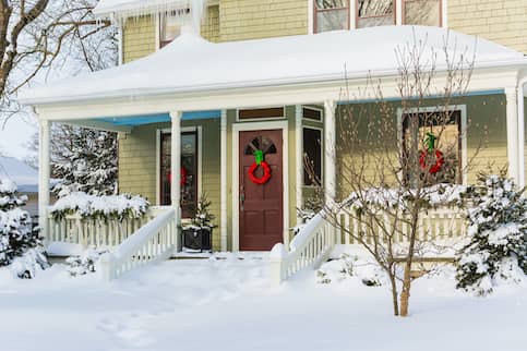 Sage Colored Home covered in snow with a Brown Door and a Red Wreath