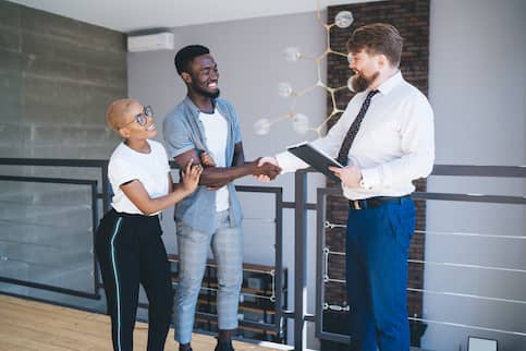 Salesman in business casual with young couple on apartment balcony and shaking hands.