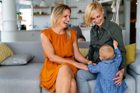 Lesbian veteran couple with toddler in living room of home. 