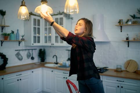 woman on a step ladder in kitchen changing lightbulb