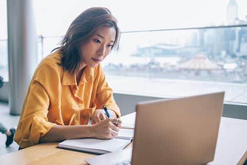 Woman on laptop and writing in notebook.