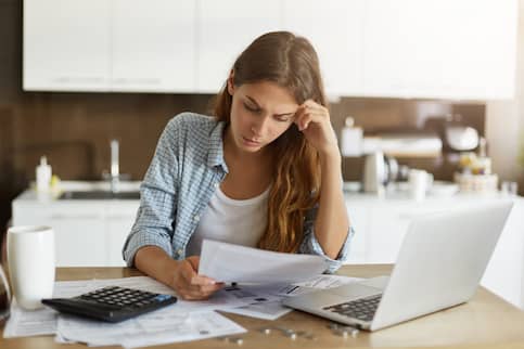woman worrying over debt looking at laptop and bills