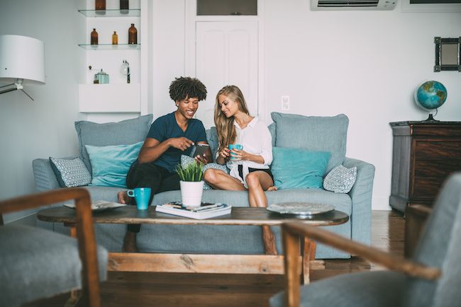 Young couple drinking coffee and laughing on couch. 