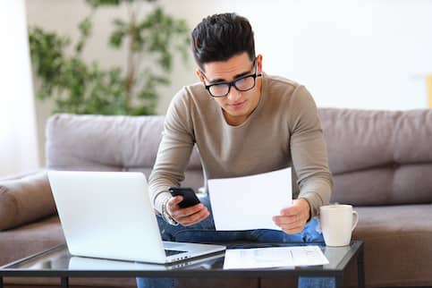 Young male with large black glasses looking at documents and his phone.