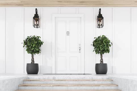 Symmetrical front door and entryway to house with potted plants and lanterns on both sides.