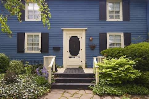 Blue house entryway and front door with bushes on each side.