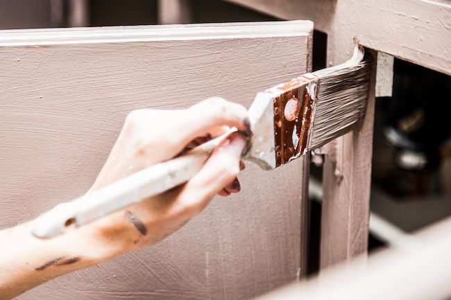 Close up shot of a hand holding a messy paintbrush, painting a cabinet.