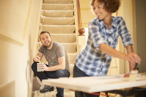 Young couple painting around their covered stairs.