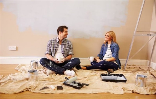 Young couple sitting on covered floor after painting.