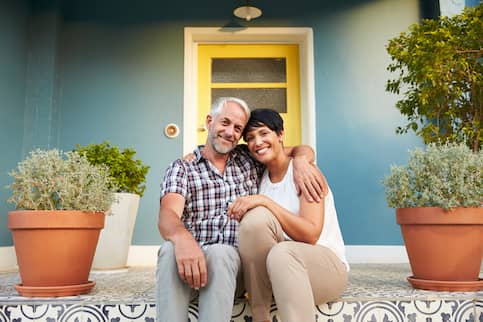 Older couple sitting on their porch in front of their front door.