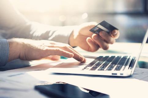 Close up shot of someone's hands holding a credit card and using a laptop.