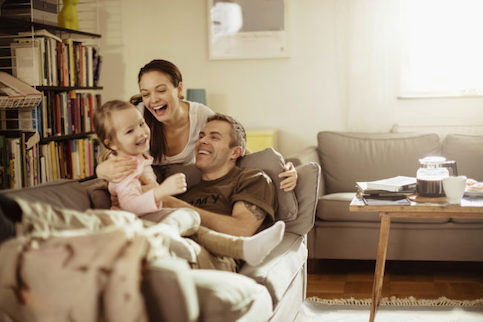 A young couple with a toddler laughing on their couch in the living room.