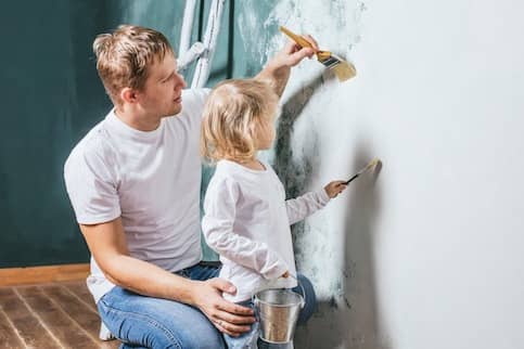 Father and daughter painting wall.