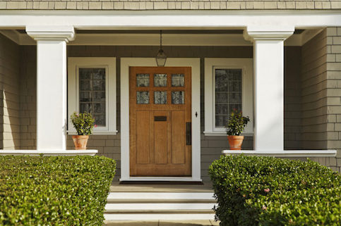 Brown front door with windows on either side and hedges out front.