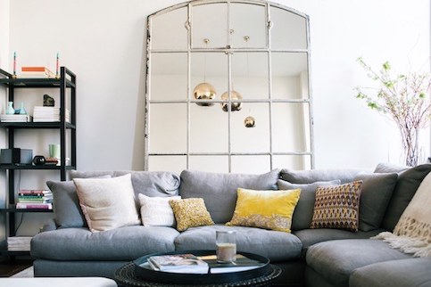 Colorful couch in living room with large mirror and round gold ceiling lights.