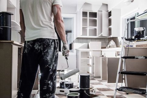 Man with a paint roller standing in a messy kitchen.