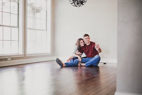 Newlywed couple sitting in empty room on the floor in their new house.