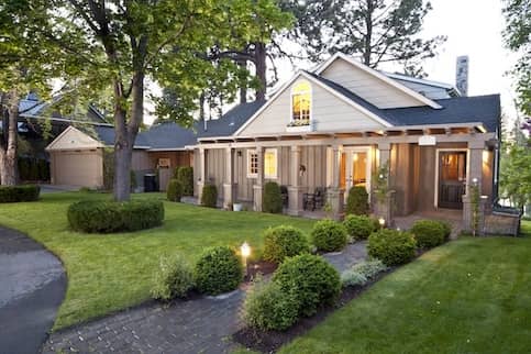 Large, rustic house with pillars and walkway leading up to it flanked by many hedges.