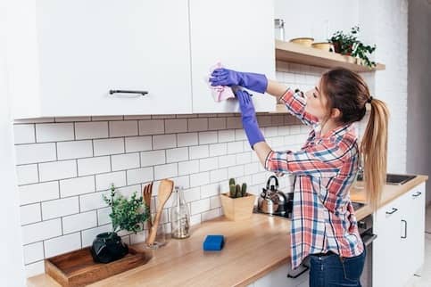 Woman cleaning her kitchen cabinets wearing purple cleaning gloves.