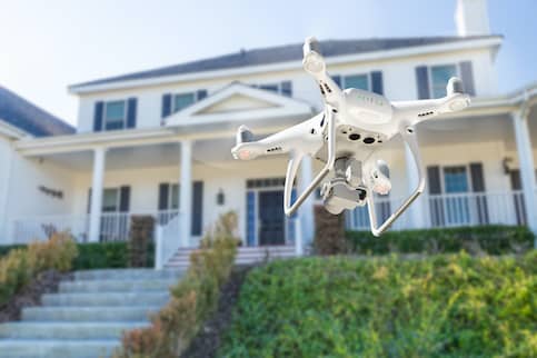 White Quadcopter Drone Taking Photos Around A White Home With Porch