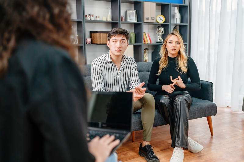 A man and woman sit on a couch, talking to a loan officer who's on her laptop.