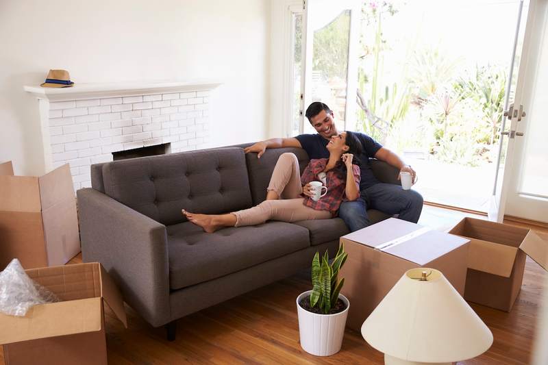 Young, happy couple, walking into room of new home, filled with moving boxes