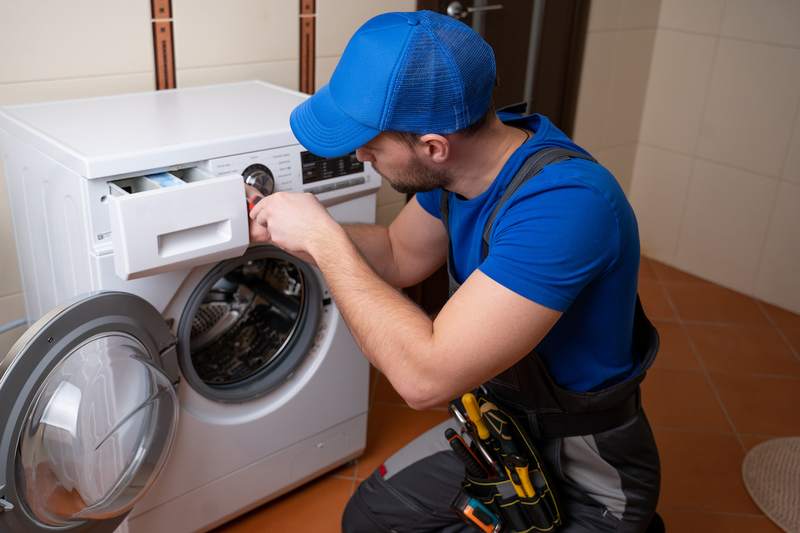 Worker repairs washing machine in laundry room.
