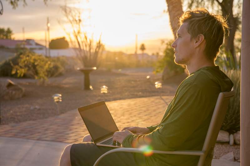 A man sits on his Arizona home's patio with a laptop during sunset.